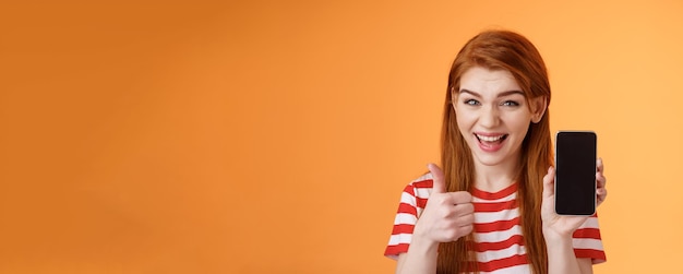 Cheerful assertive redhead woman recommend smartphone app show phone display thumbup like approval s