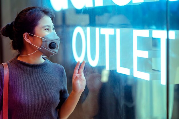 Cheerful attractive asian female woman wearing protective face mask looking at outlet sale signage shopfront window display new normal lifestyle concept