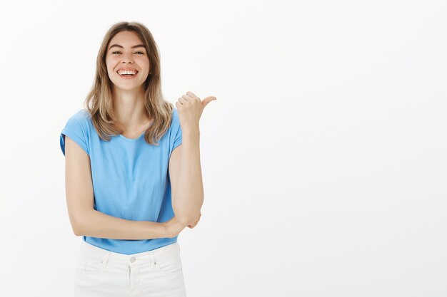 Cheerful attractive woman pointing finger right, showing way