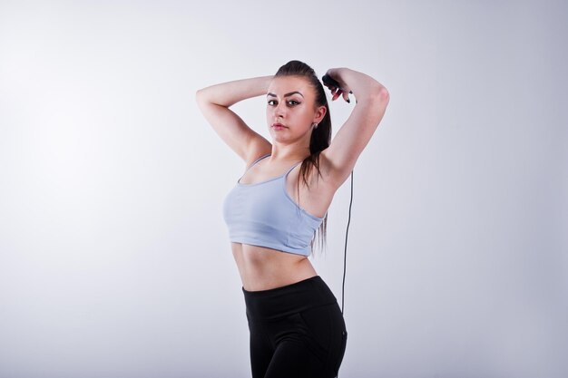 Cheerful attractive young fitness woman in top and black leggings with jump rope isolated over white background