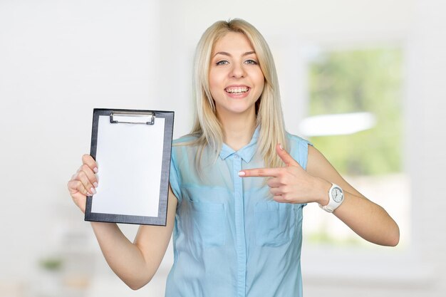 Cheerful attractive young woman showing blank clipboard