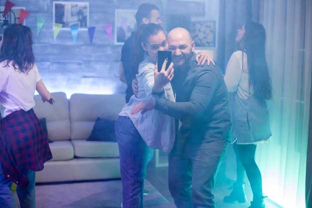 Free photo cheerful bald man taking a selfie with his girlfriend at the party.