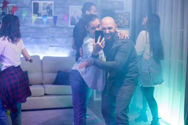 Cheerful bald man taking a selfie with his girlfriend at the party.