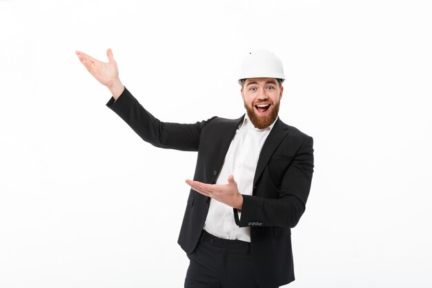 Cheerful bearded business man in protective helmet pointing away