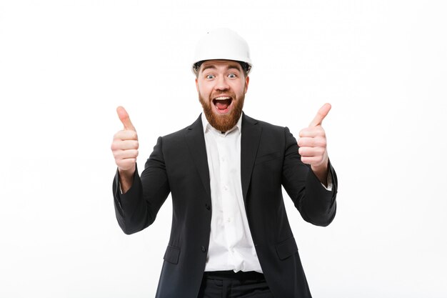 Веселый бородатый деловой человек в защитном шлеме показывает палец вверх