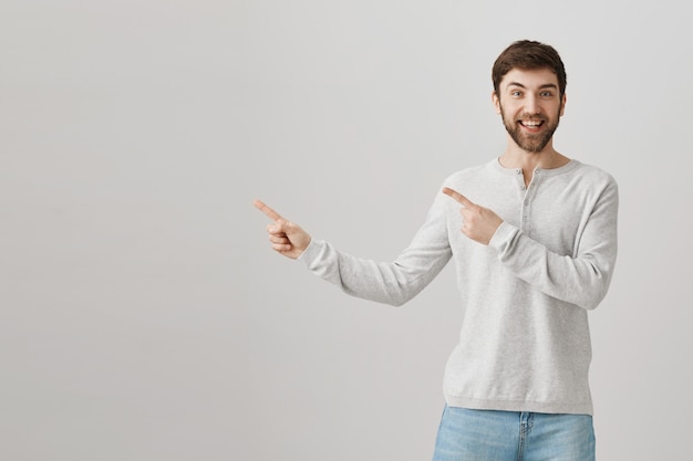 Cheerful bearded caucasian guy pointing fingers left