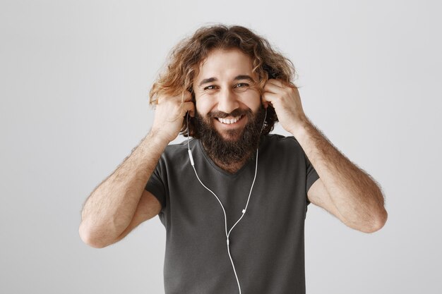 Cheerful bearded guy put on earphones and smiling happy, listening music