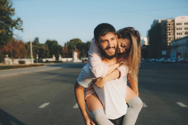 Cheerful bearded man carrying young woman on back while walking on street in leisure