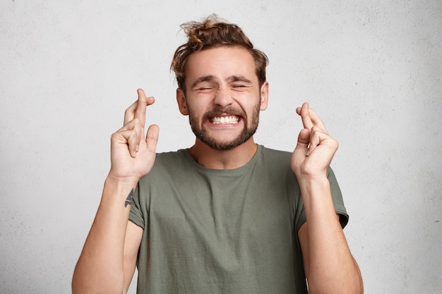 Free photo cheerful bearded man keeps fingers crossed, smiles broadly and closes eyes