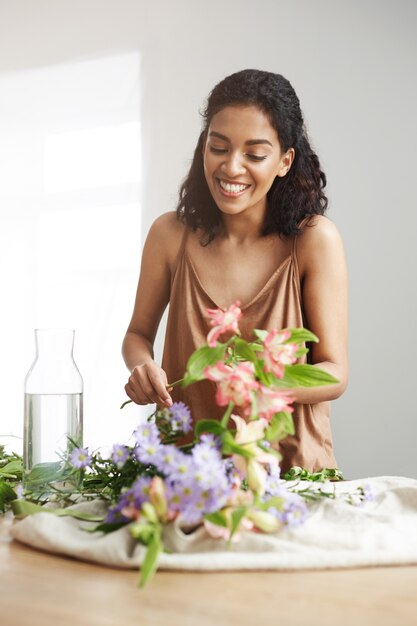 흰 벽에 직장에서 꽃다발을 만드는 웃 고 밝고 아름 다운 아프리카 꽃집.