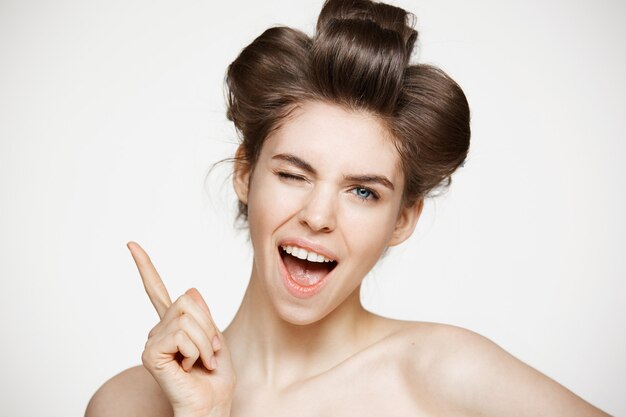 Cheerful beautiful woman in hair curlers smiling with opened mouth winking.