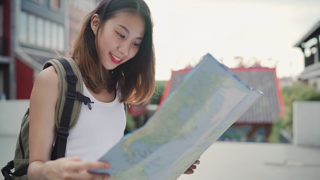 Веселая красивая молодая азиатская рюкзаком женщина направление и глядя на карту местности