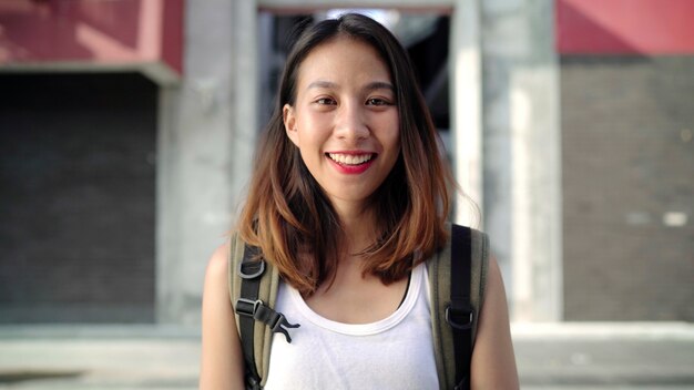 Cheerful beautiful young Asian backpacker woman feeling happy smiling to camera 