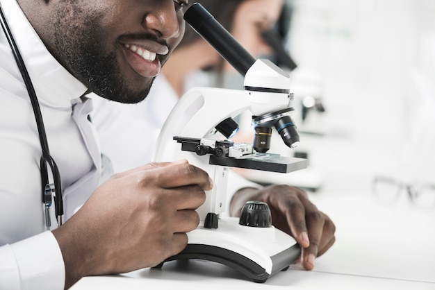 Cheerful black medic using microscope 
