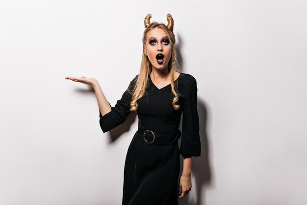 Cheerful blonde girl with black makeup posing in halloween.  fascinating female vampire isolated on white wall.