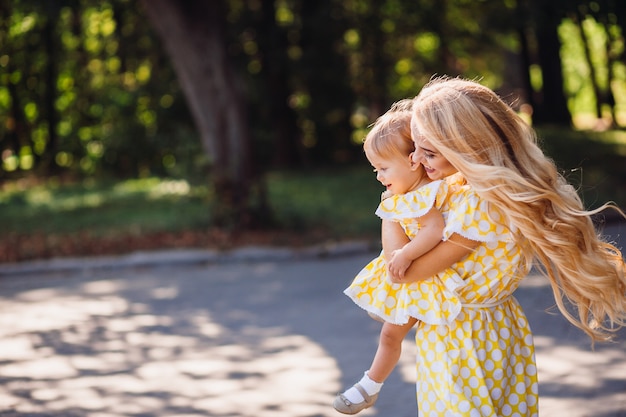 Веселая блондинка мама ходит с маленькой девочкой в ​​парке