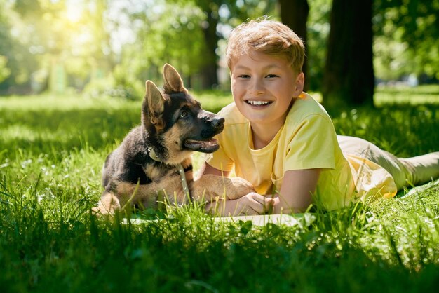 Веселый мальчик и щенок немецкой овчарки играют в парке