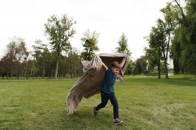 Free photo cheerful boy running with a flying blanket in the park