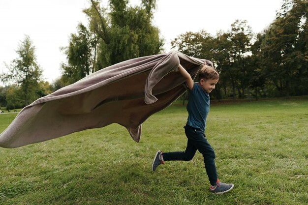 Cheerful boy running with a flying blanket in the park