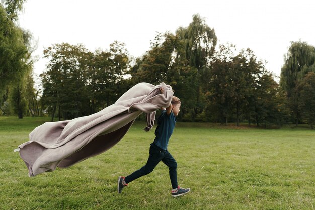 Cheerful boy running with a flying blanket in the park