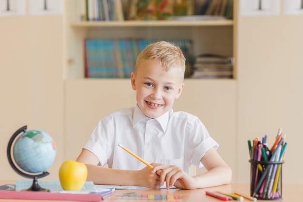 Foto gratuita ragazzo allegro che si siede allo scrittorio della scuola