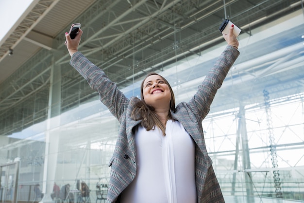 Cheerful business woman raising arms outdoors