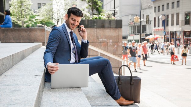 Веселый бизнесмен, разговариваете по телефону и используя ноутбук