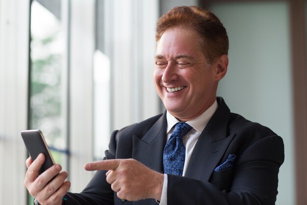 Cheerful businessman using cellphone and laughing