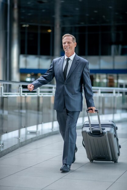 Cheerful businessman wheeling his baggage through the airport terminal