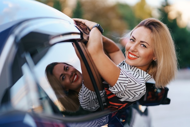 陽気な白人女性は美しい日当たりの良い街をドライブし、美しい日に車の窓からストレッチしながら腕を振る