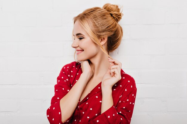 Cheerful caucasian young woman playfully posing on white wall. Indoor shot of european girl enjoying photoshoot in good day.