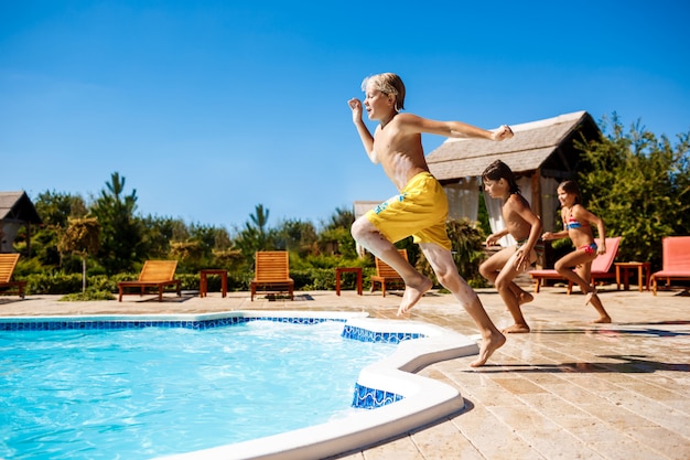 Cheerful children rejoicing, jumping, swimming in pool.