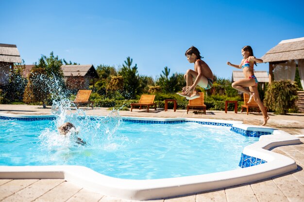 Cheerful children rejoicing, jumping, swimming in pool.