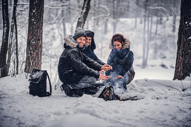 Cheerful company of students basking near a campfire in a snowy forest in winter