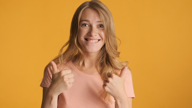 Cheerful cool blond girl keeping thumbs up joyfully looking in camera isolated on yellow background Like expression