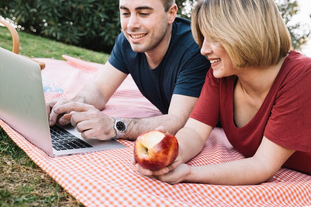 Computer portatile di lettura rapida delle coppie allegre sul picnic