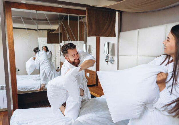 Cheerful couple have fun in the bedroom fighting with big pillows at home