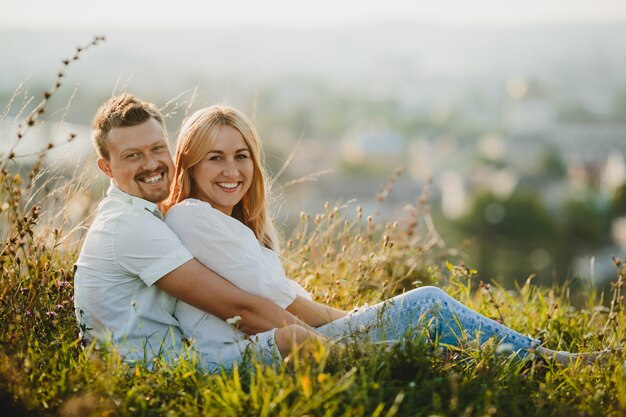 Cheerful couple hugs each other tender sitting on the green lawn in beautiful summer day