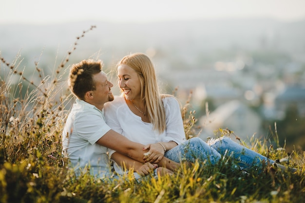 Cheerful couple hugs each other tender sitting on the green lawn in beautiful summer day