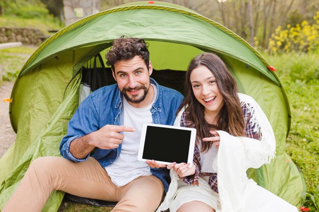 タブレットを指すテントの近くの陽気なカップル