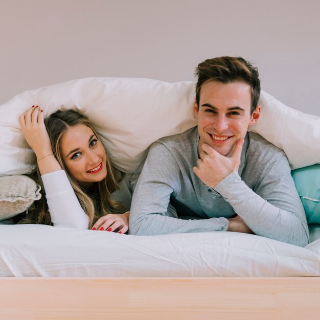 Cheerful couple posing under blanket