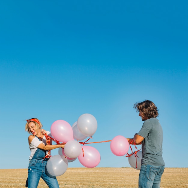 Free photo cheerful couple pulling balloons