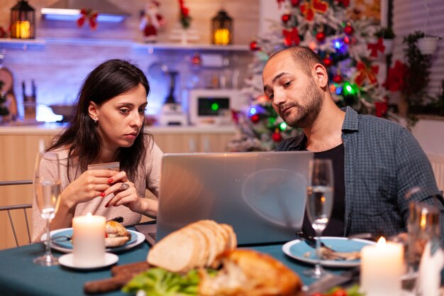 신용 카드로 지불하는 온라인 크리스마스 선물을 쇼핑하는 쾌활한 커플
