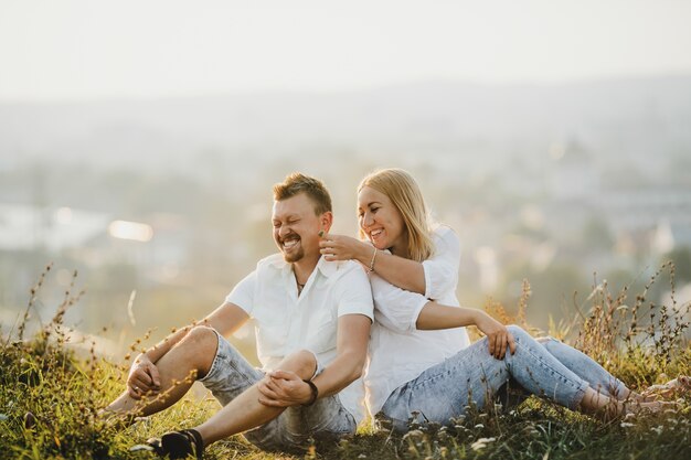 Cheerful couple sits side by side on the green lawn in beautiful summer day