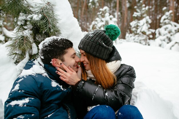 Cheerful couple sitting on the snow under the tree. Winter.