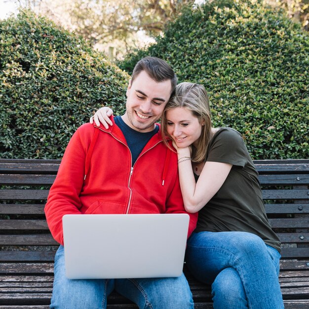 Cheerful couple using laptop on bench