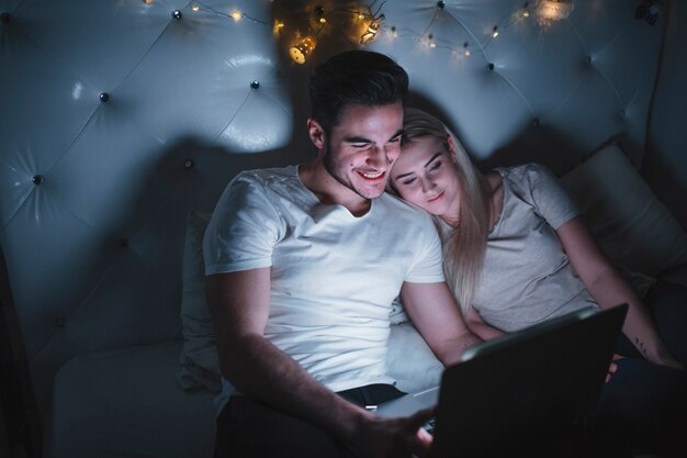 Cheerful couple watching movie on bed