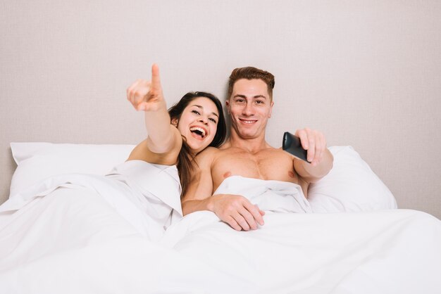 Cheerful couple watching tv in bed