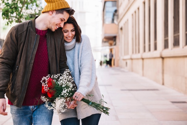 Cheerful couple with bouquet walking down street