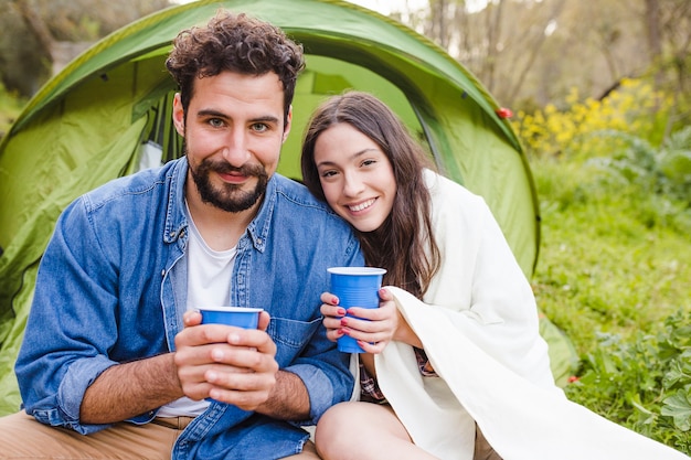 Cheerful couple with cups near tent
